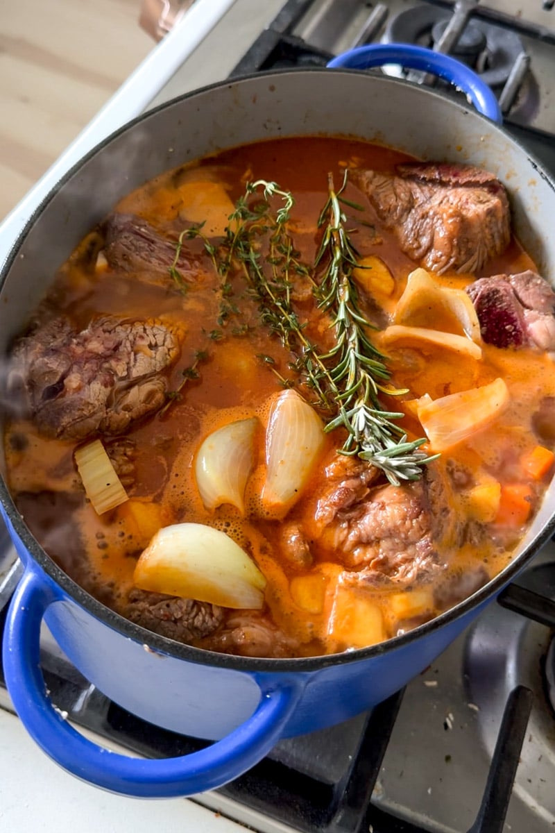 short ribs and veggies and braising liquid in a blue dutch oven.