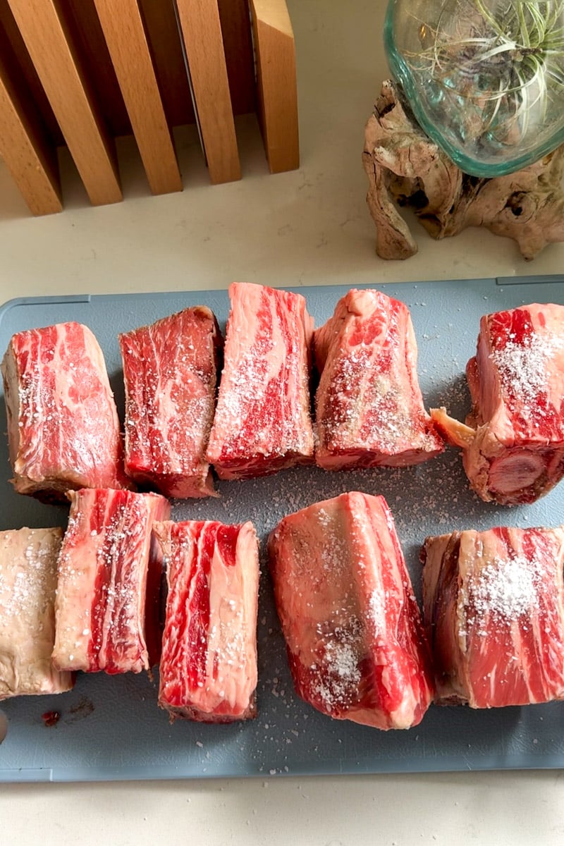 short ribs with salt, pepper and garlic powder on a blue cutting board.