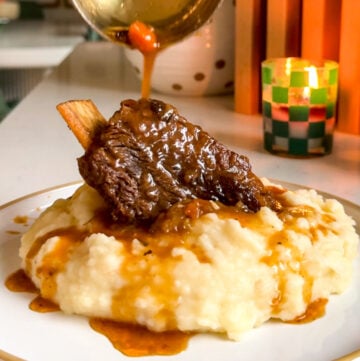 a braised chuck beef short rib with gravy on a white plate.