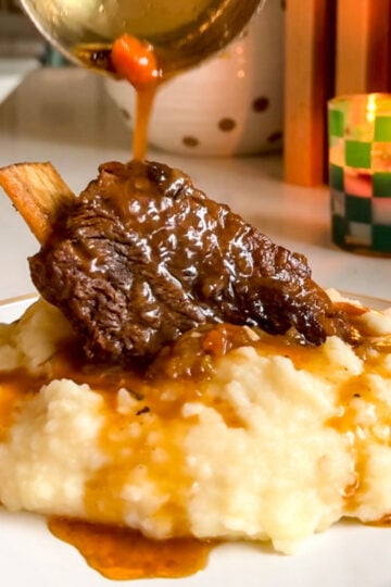 a braised chuck beef short rib with gravy on a white plate.