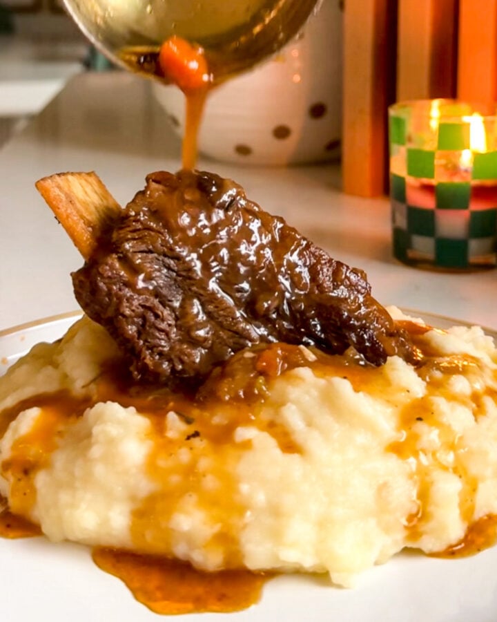 a braised chuck beef short rib with gravy on a white plate.