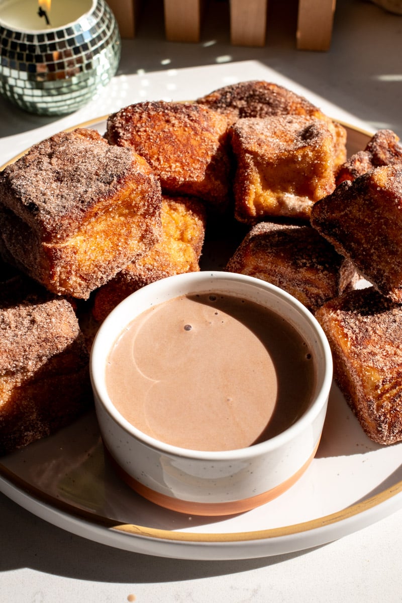 a white ramekin filled with hot chocolate dipping sauce in front of hot chocolate french toast bites.