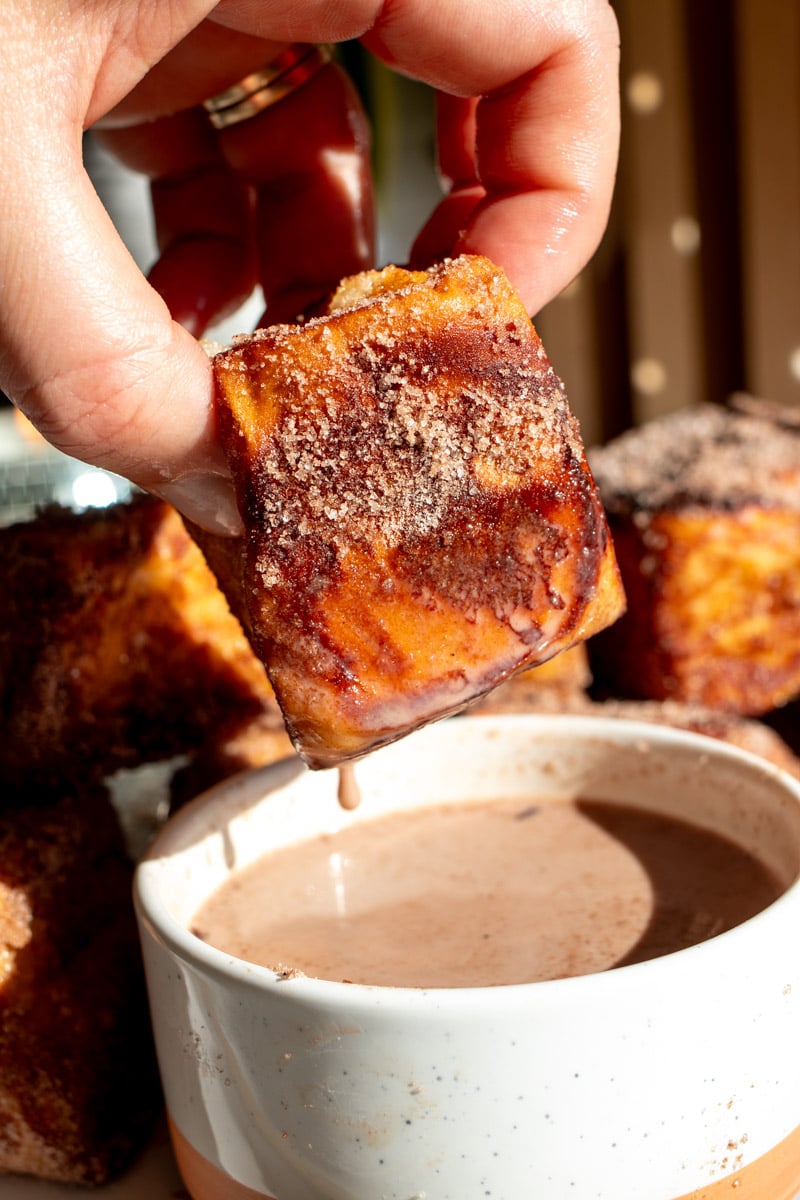 a hand holding a piece of hot chocolate french toast being dunked in hot chocolate dipping sauce. 