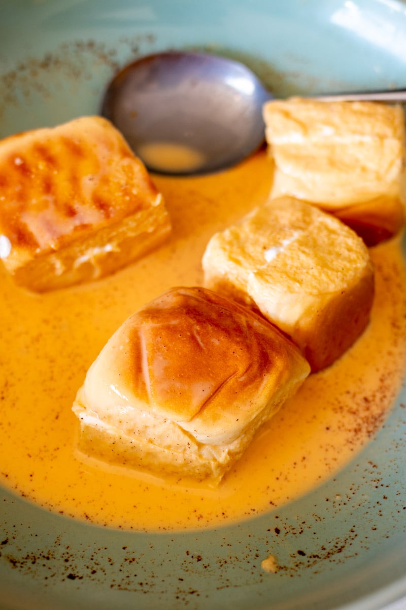 hawaiian rolls soaking in custard in a blue bowl.