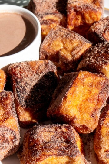 a white plate of hot cocoa french toast bites with a hot chocolate dipping sauce.