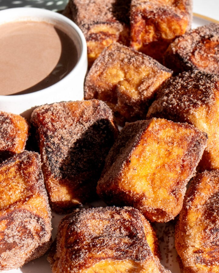 a white plate of hot cocoa french toast bites with a hot chocolate dipping sauce.