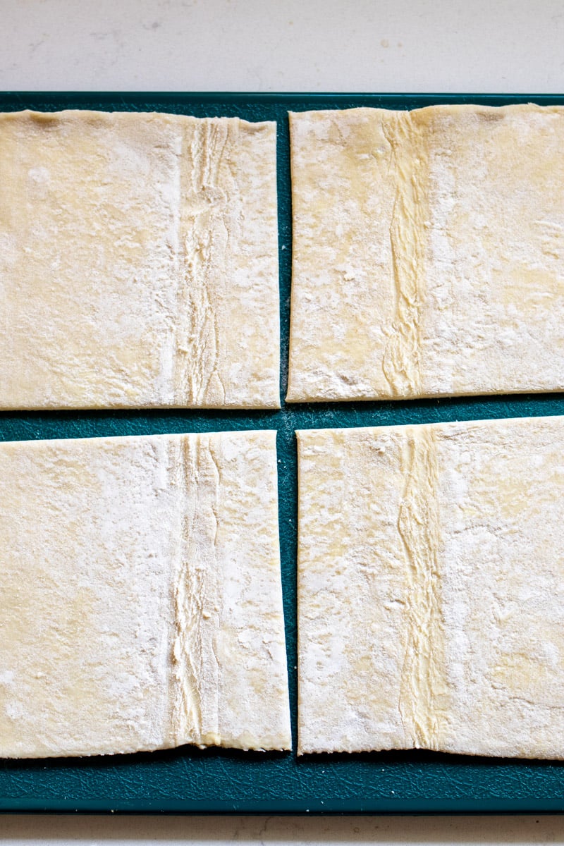 puff pastry cut into four squares on a blue cutting board.