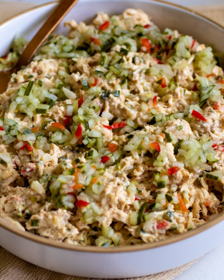 dill pickle chicken salad in a white bowl with a golden spoon.