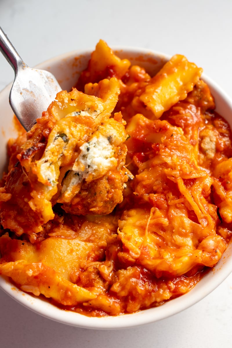 a small white bowl filled with lasagna made from ravioli and store bought meatballs.