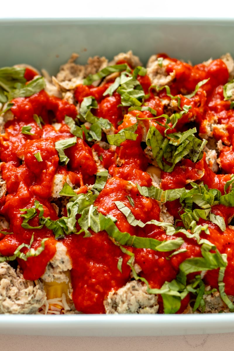 basil, tomato sauce, meatballs and ravioli in a blue baking dish.