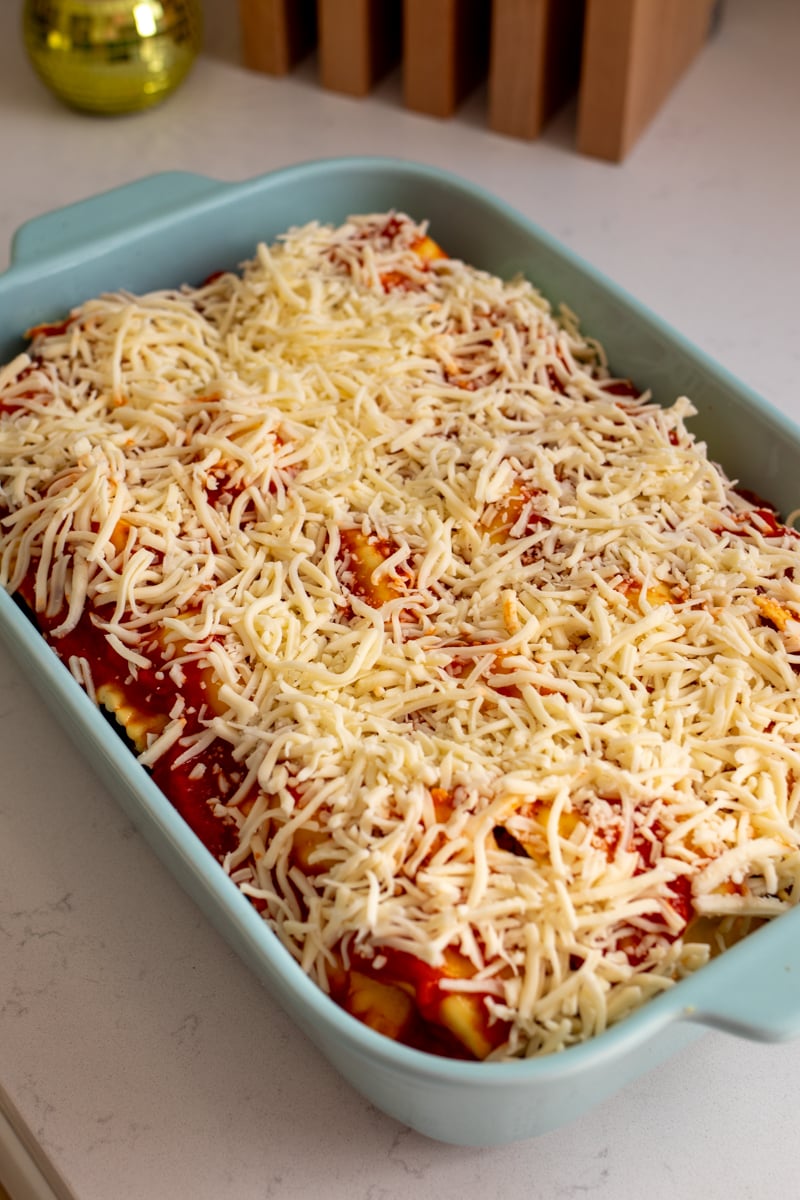 a blue baking dish filled with ravioli, mozzarella, meatballs and tomato sauce. 