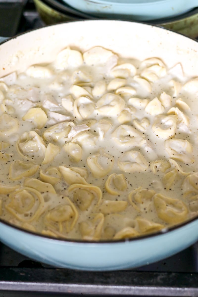 fresh cheese tortellini being cooked in a milk and heavy cream mixture.