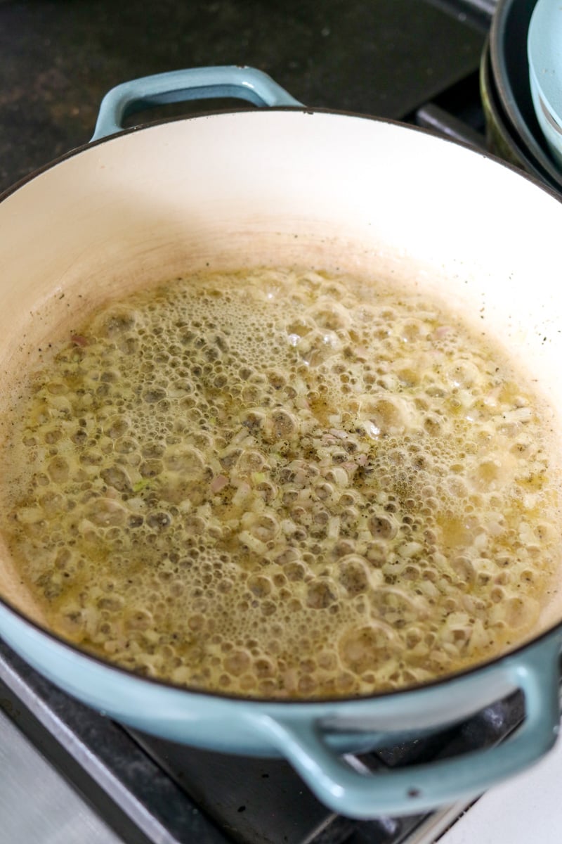 Butter, shallots, and seasoning cooking in a blue braising pot.
