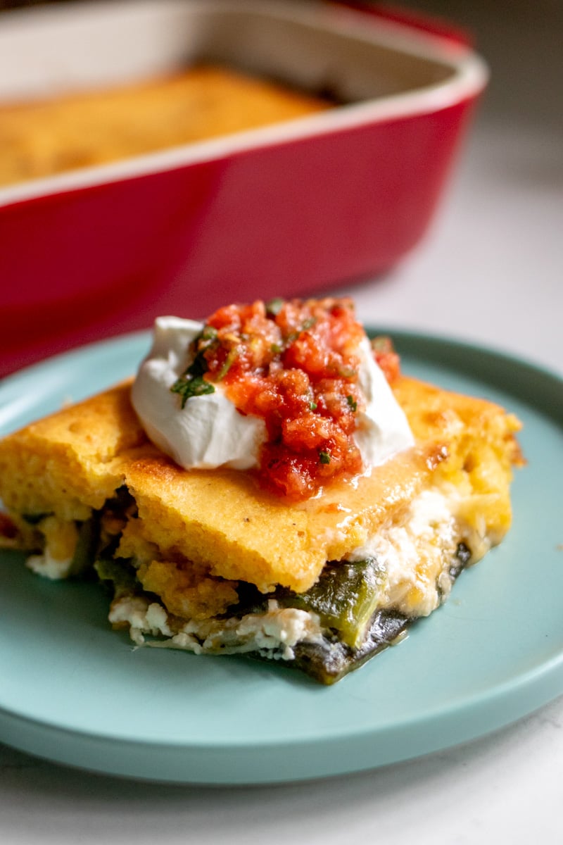 a slice of chile relleno casserole on a blue plate with the baking dish behind it.  