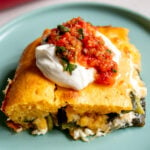 a slice of chile relleno casserole topped with sour cream and salsa on a blue plate.