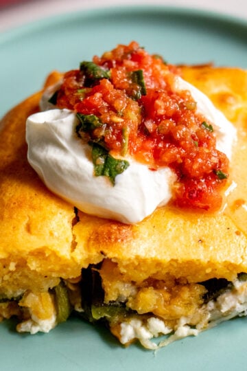 a slice of chile relleno casserole topped with sour cream and salsa on a blue plate.