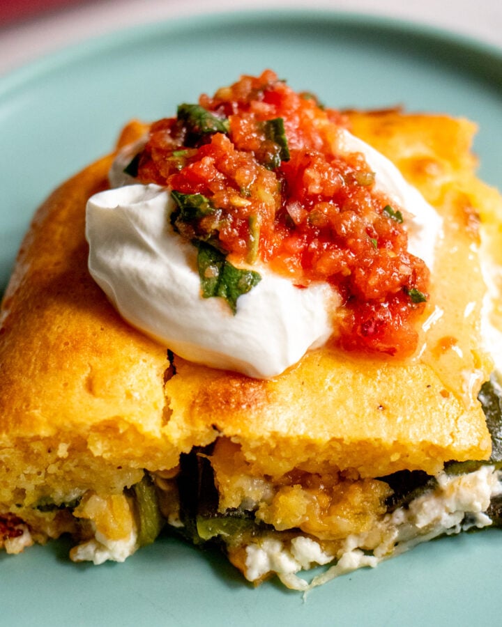 a slice of chile relleno casserole topped with sour cream and salsa on a blue plate.