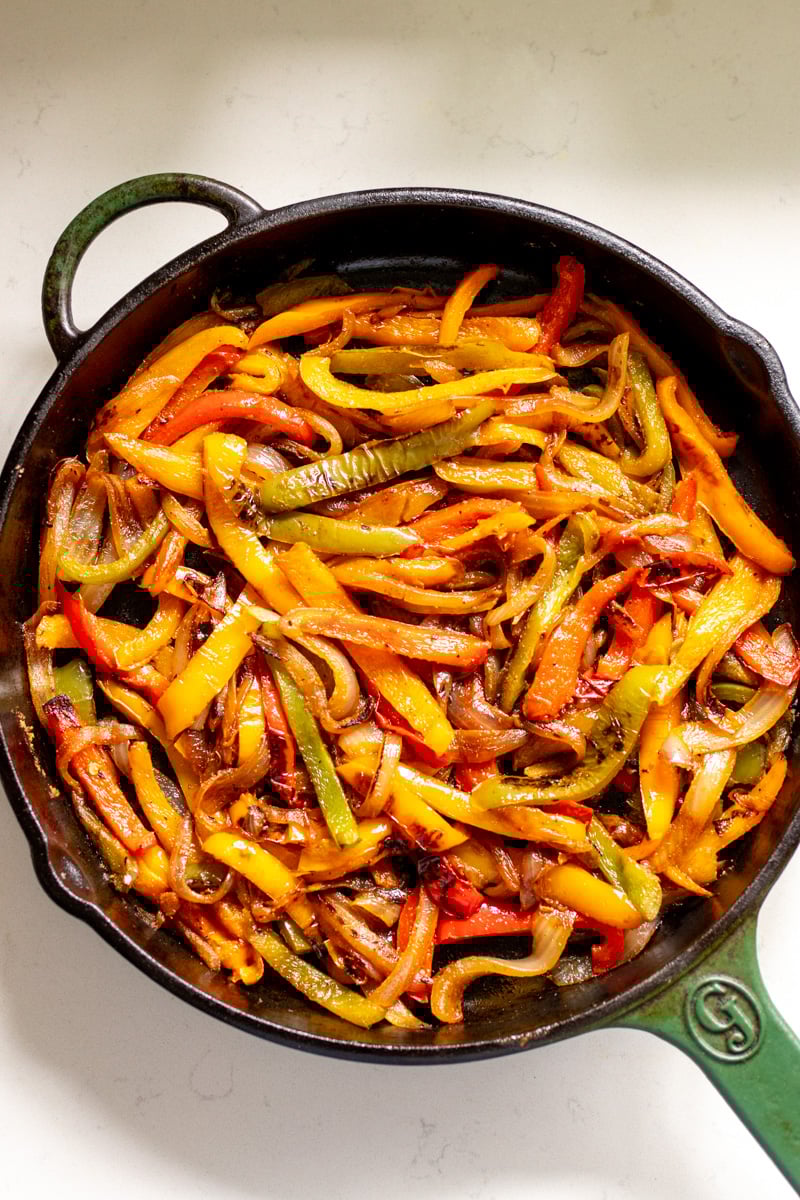 an overhead view of a big cast iron skillet full of fajita veggies on a white countertop.