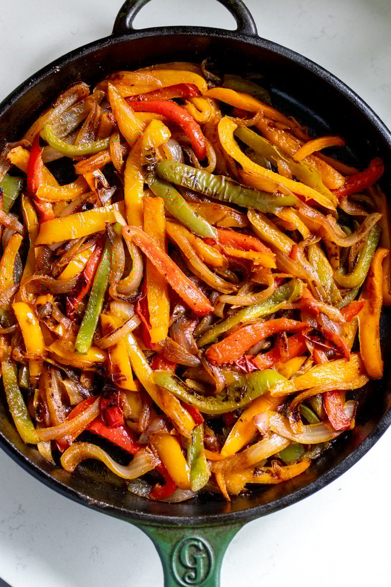 fajita veggies being cooked in a large green skillet.