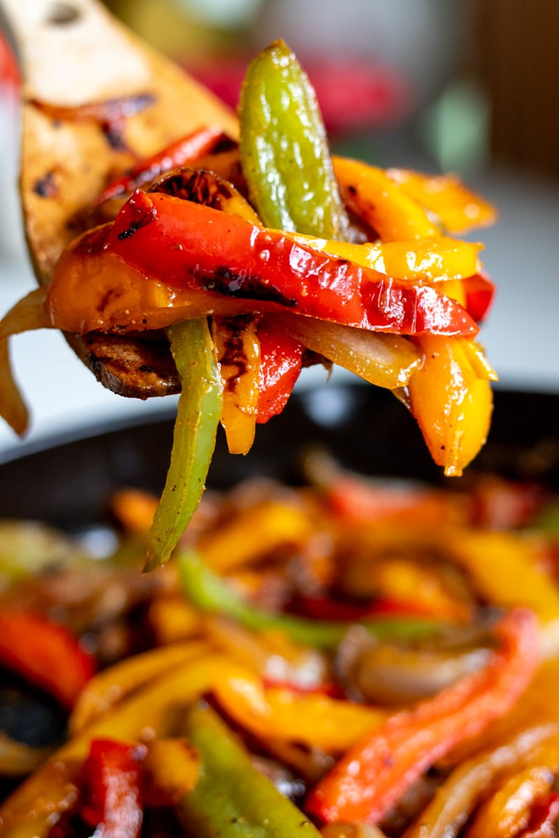 a spatula holding a scoop of fajita veggies over the cooking pan.