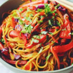 bright yellow singapore street noodles in a green bowl with lots of colorful veggies.