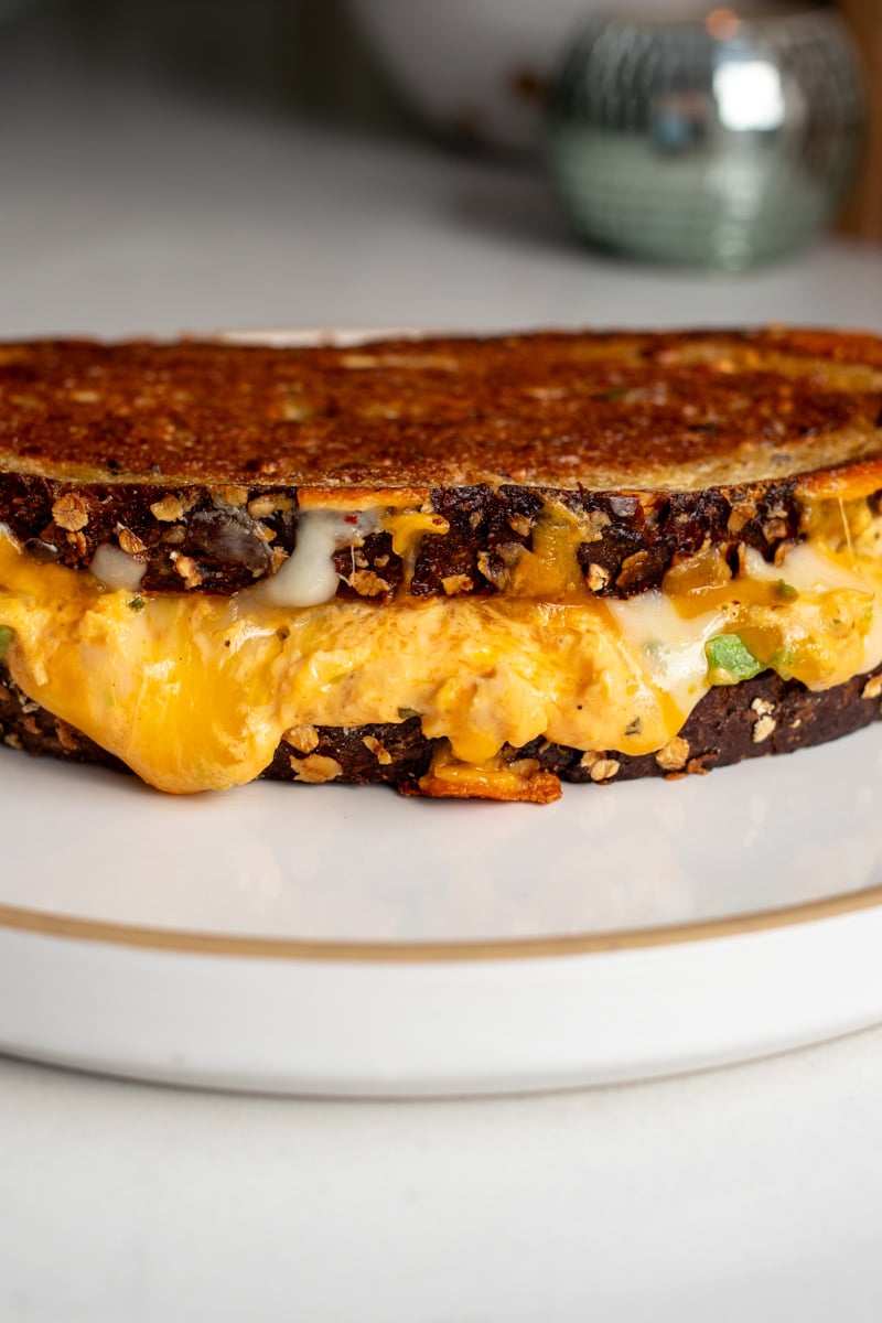 a buffalo chicken dip avocado grilled cheese on a white plate with cheese oozing out of it.