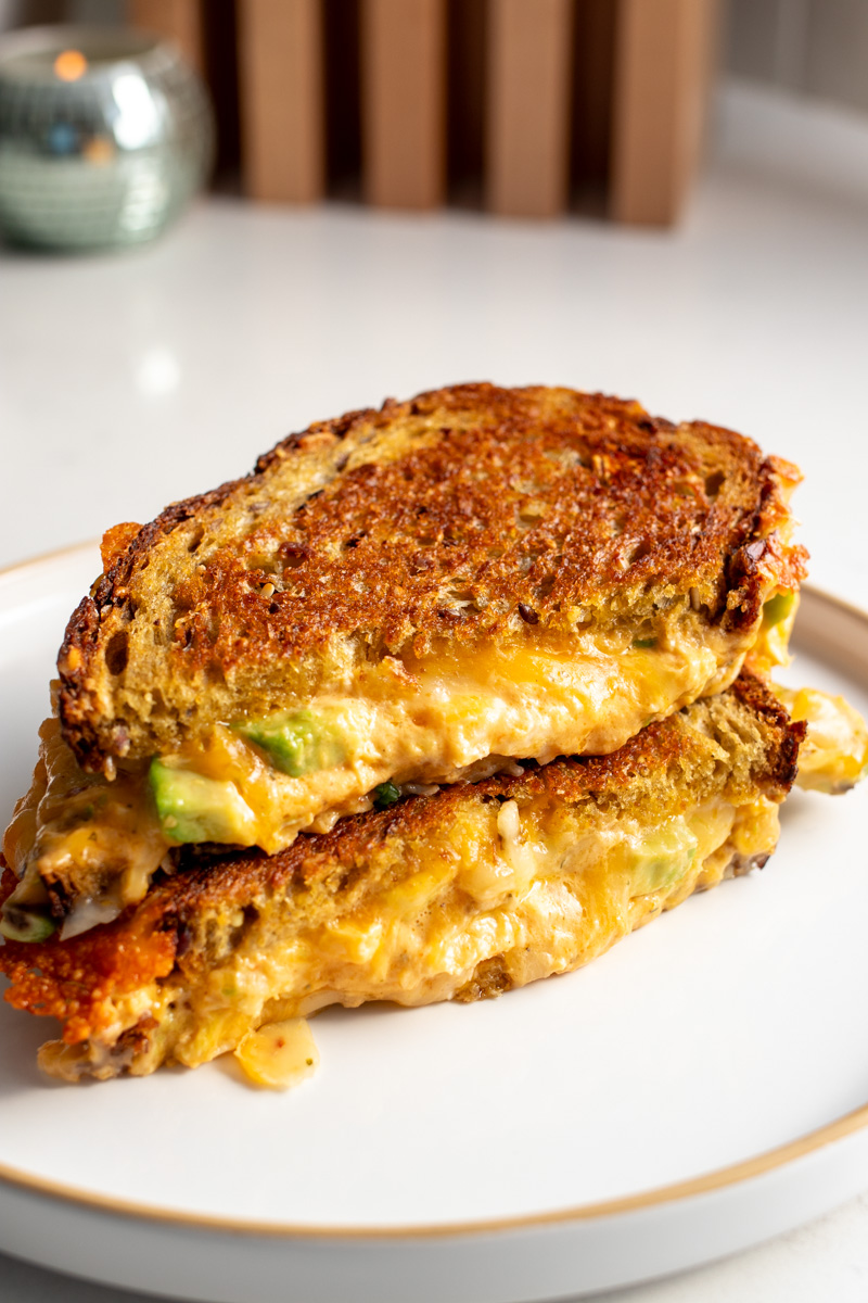 cheesy buffalo chicken dip and avocado oozing out of a plated grilled cheese sandwich. 