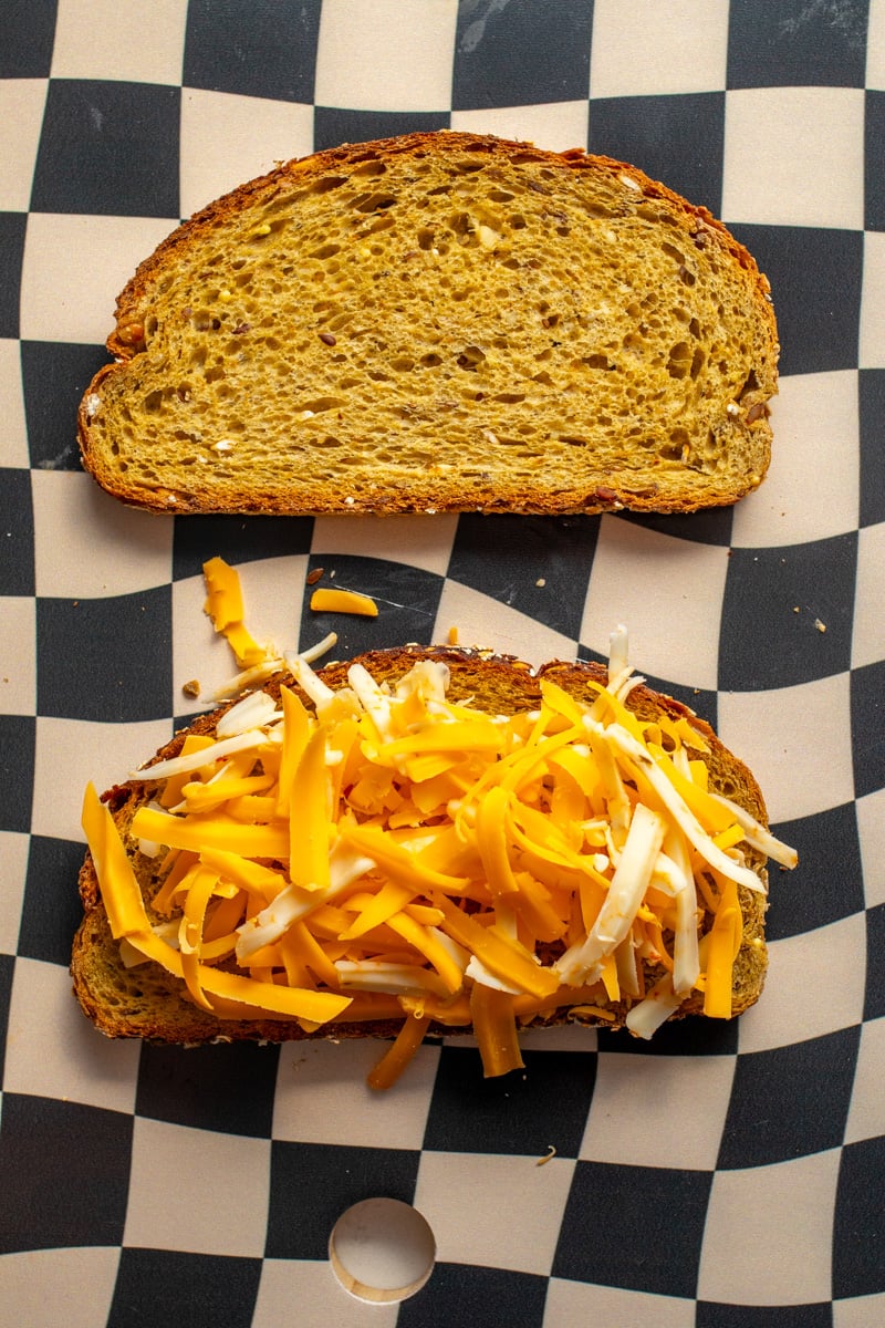 shredded cheese on a slice of toast on a cutting board.