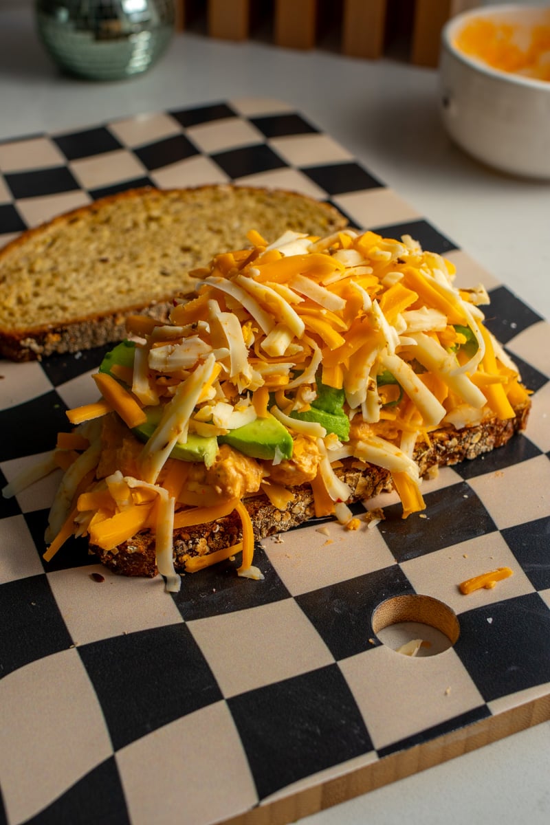 shredded cheese on top of an open faced grilled cheese sandwich.