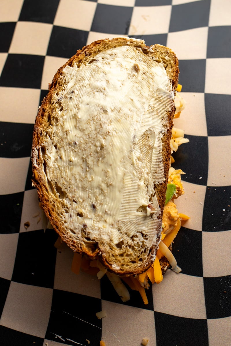 an overhead view of a built grilled cheese sandwich smeared with butter.