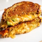 a buffalo chicken dip grilled cheese with avocado sliced in half on a white plate.