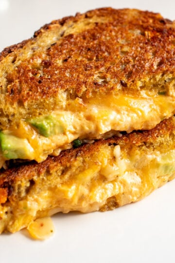 a buffalo chicken dip grilled cheese with avocado sliced in half on a white plate.