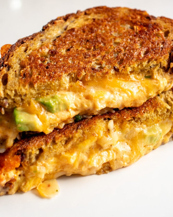 a buffalo chicken dip grilled cheese with avocado sliced in half on a white plate.