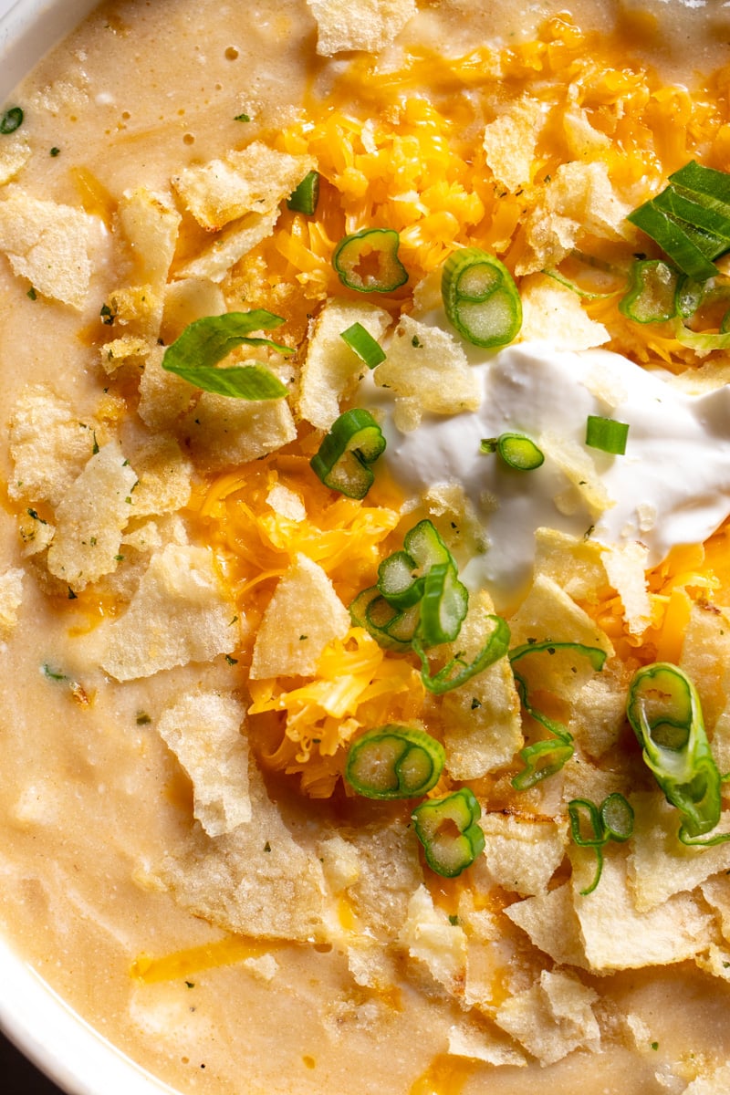 an up close view of the texture of this creamy soup with potatoes, cheese, scallions and sour cream and onion chips.