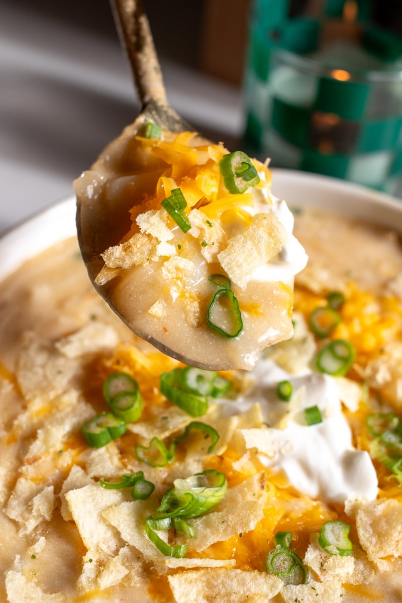 a golden spoon holding a scoop of cheesy potato soup over a bowl.