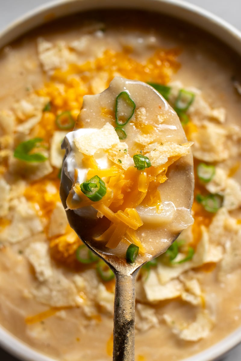 a golden spoon holding a big loaded scoop of cheesy potato soup over the serving bowl.