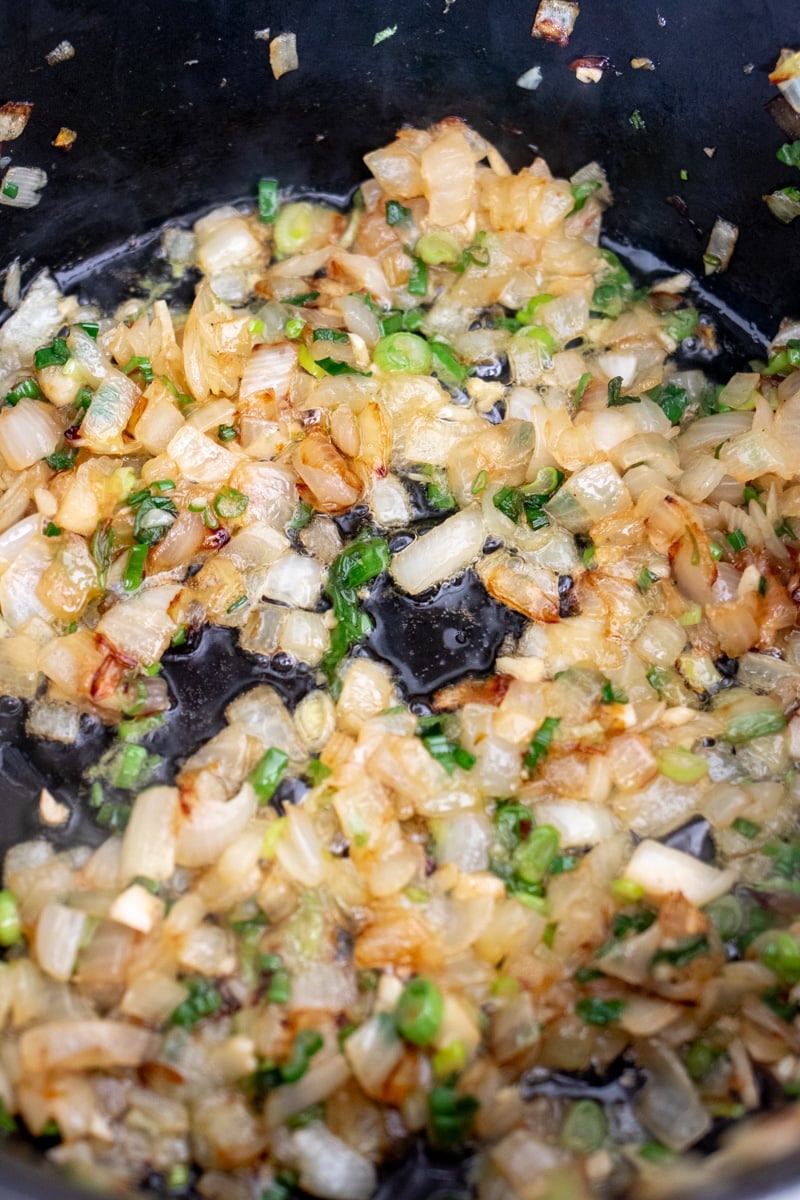 onions, scallions and garlic being cooked in butter and olive oil in a large dutch oven.