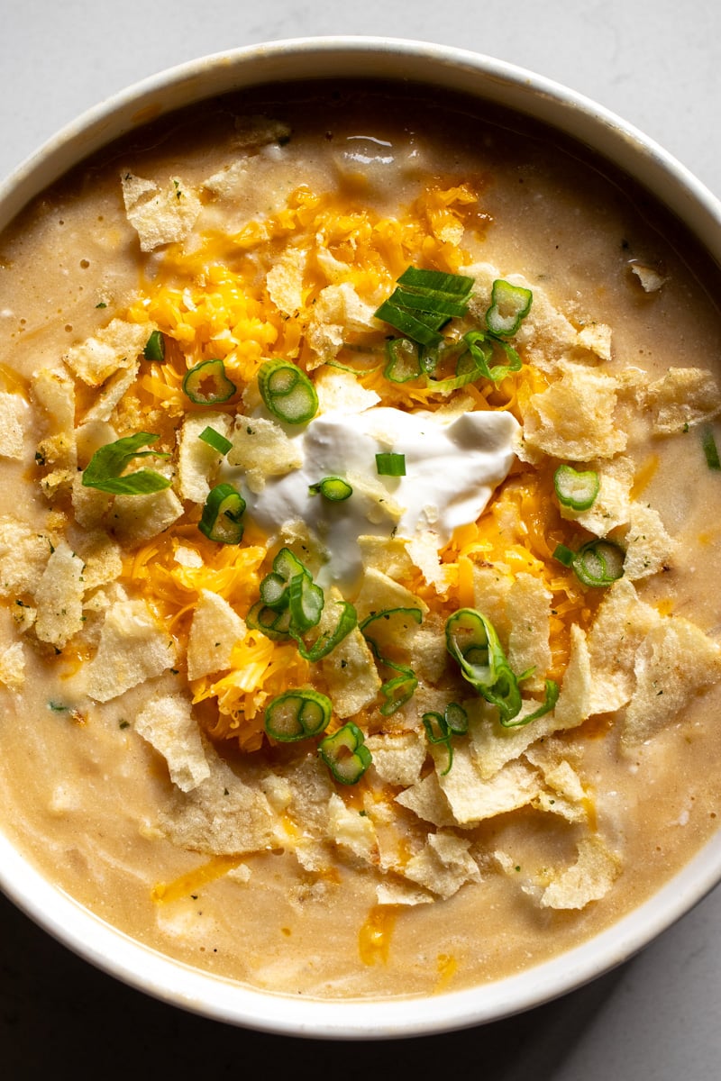 a white bowl filled with creamy potato soup loaded with cheddar cheese, sour cream and scallions. 