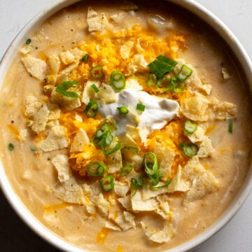 a white bowl filled with cheesy potato soup that's topped with cheddar, green onions and sour cream and onion potato chips.