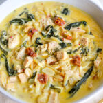 a white bowl full of creamy chicken florentine soup with bits of orzo, tomato and spinach peeking out.