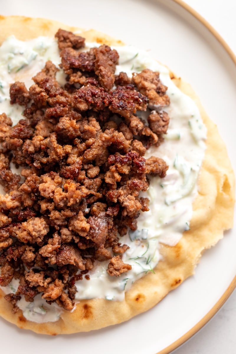 a pita with tzatziki, and ground lamb sitting on a white plate.