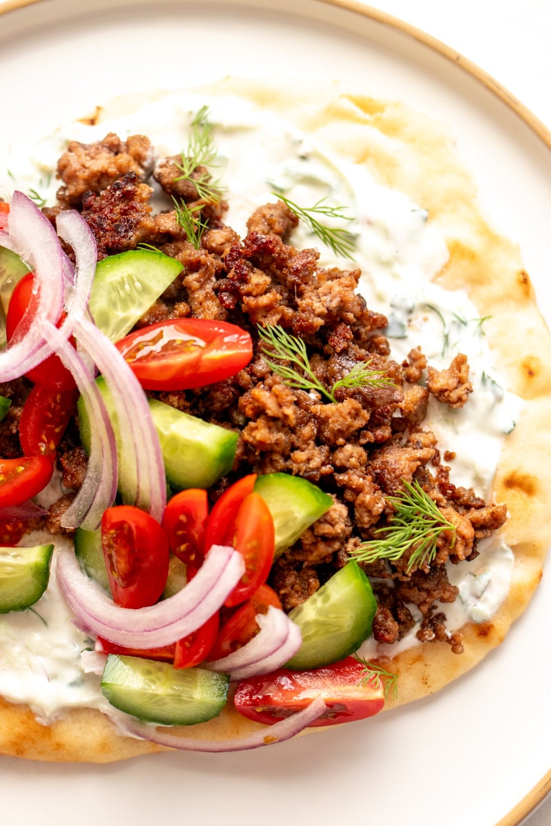 a pita topped with ground lamb gyro meat, white sauce, and colorful fresh veggies.