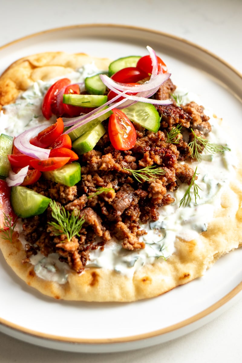 all the ingredients of a lamb gyro on a piece of toasted pita bread on top of a white plate.