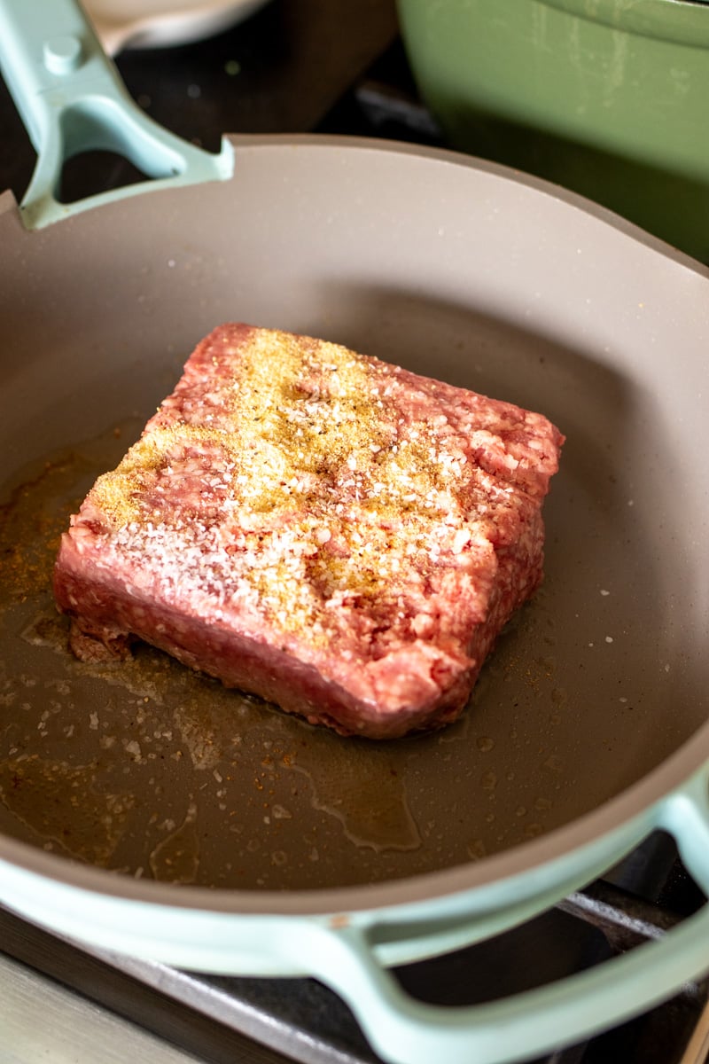 a block of ground lamb with herbs and spice on it in a frying pan.