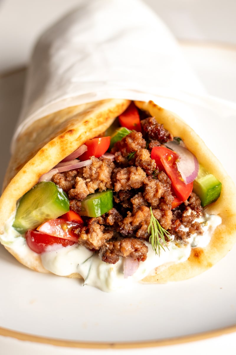 a ground lamb pita sitting on a white plate full of colorful veggies.