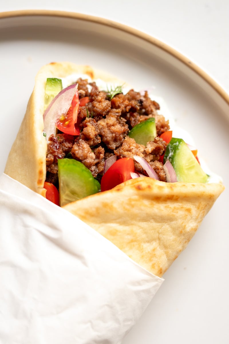 an overhead view of a wrapped up lamb gyro on a white plate.