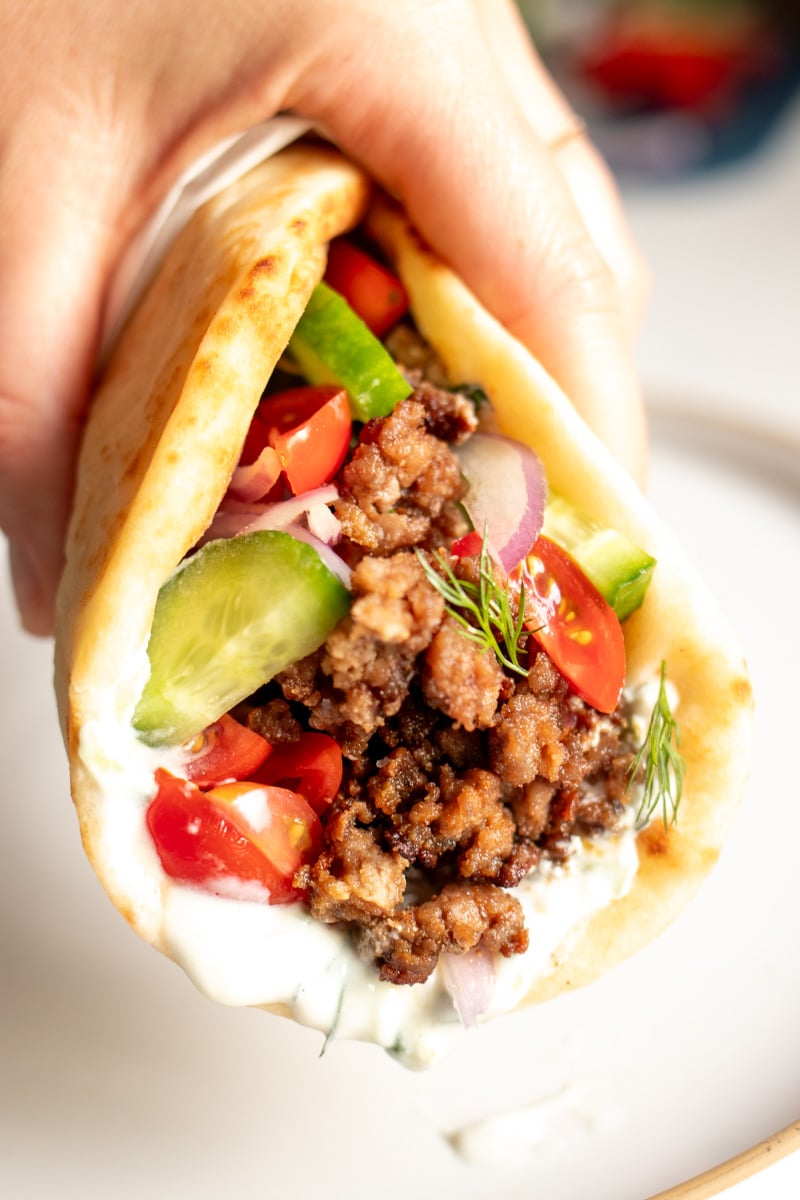 a hand holding a ground lamb gyro with tzatziki sauce dripping off of it.