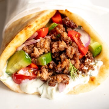 the view of the front of a ground lamb pita with tzatziki sauce, tomatoes, onions and cucumbers.