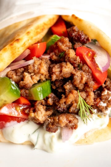 the view of the front of a ground lamb pita with tzatziki sauce, tomatoes, onions and cucumbers.