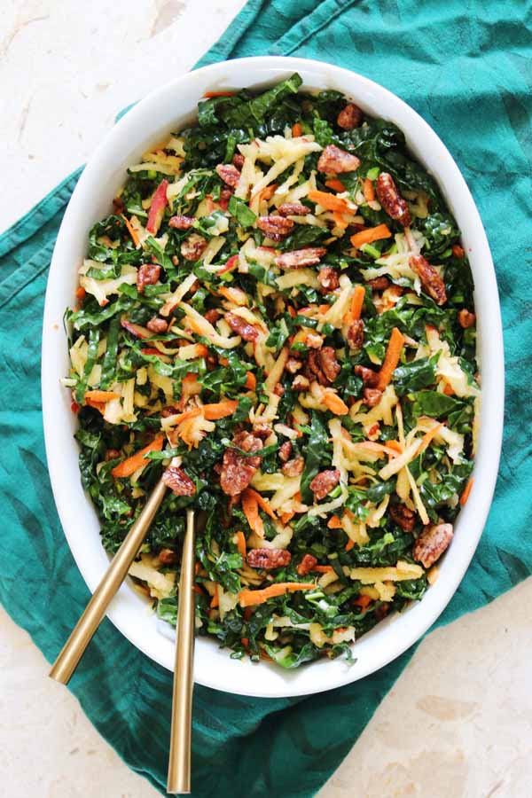 a big white serving dish filled with colorful kale apple slaw.